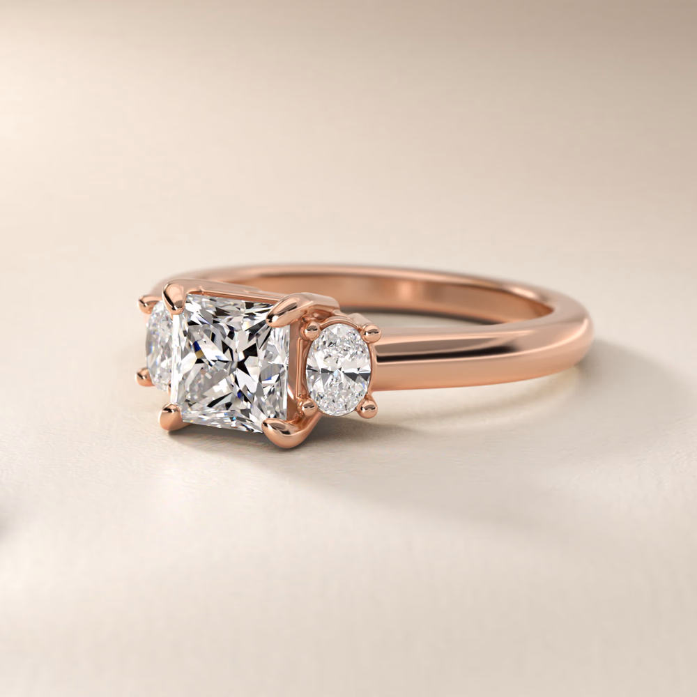 East-West Sidestone and Pavé Engagement Ring in 14K Rose Gold — princess cut center diamond with east-west oriented side stones and pavé band, rose gold creates warm pink frame for three-stone arrangement
